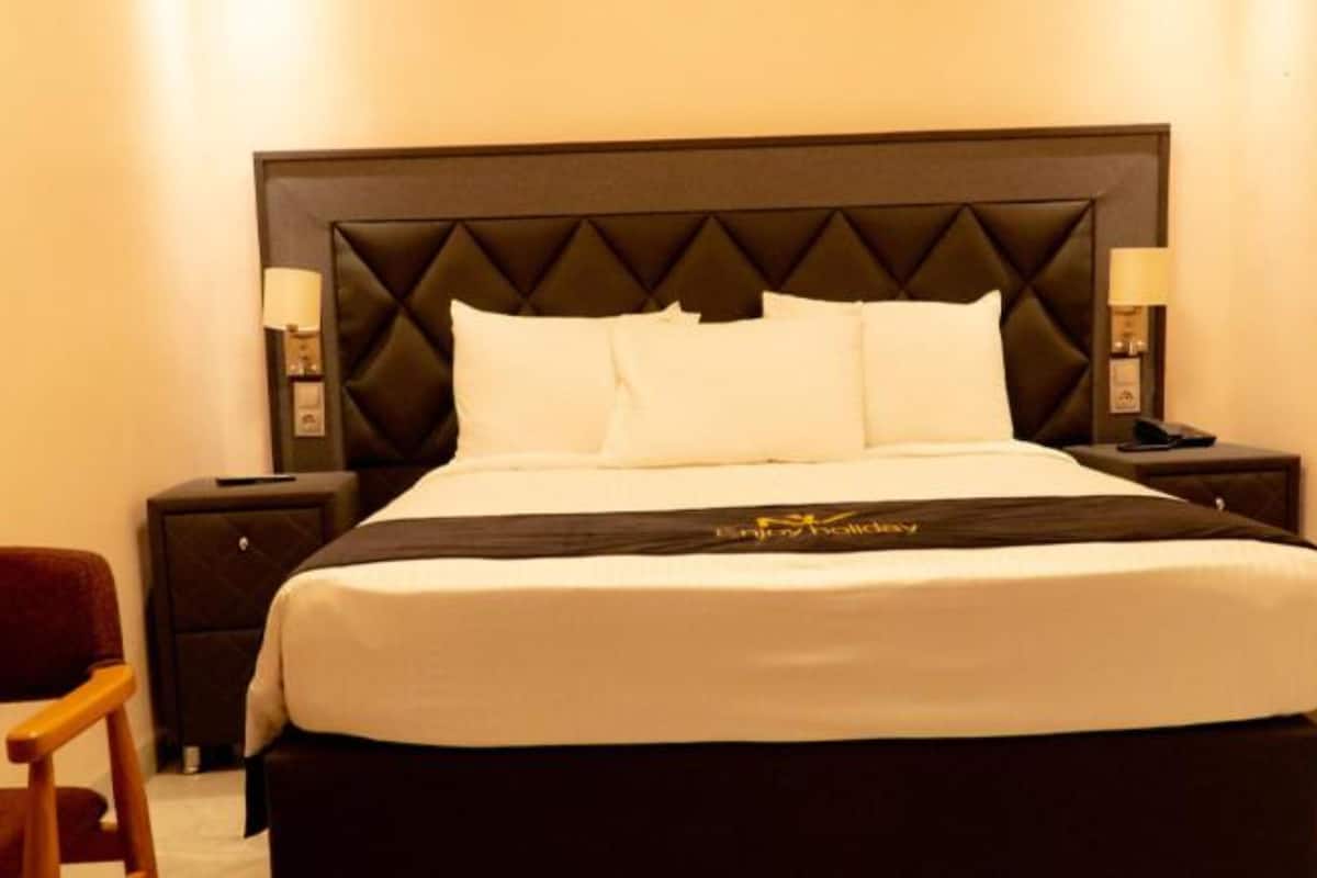 A hotel room with a large bed, two bedside tables, a chair, and a headboard with a diamond pattern.
