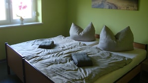 Un lit avec des oreillers, une fenêtre avec une plante et un tableau accroché au mur.