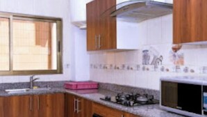 A kitchen with wooden cabinets, a gas stove, a microwave, and a window. - Loumia Residency 3ch (Douala)