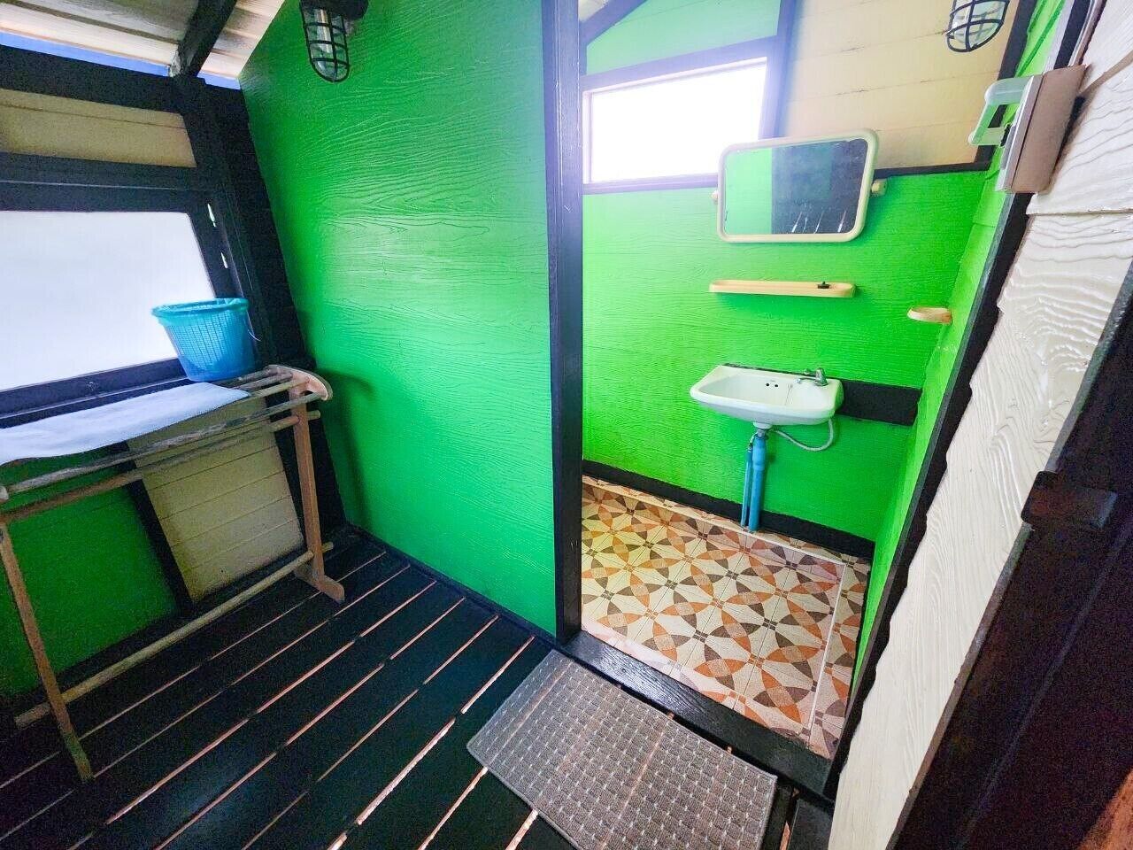 A small, compact bathroom with green walls, a tiled floor, a sink, and a window.