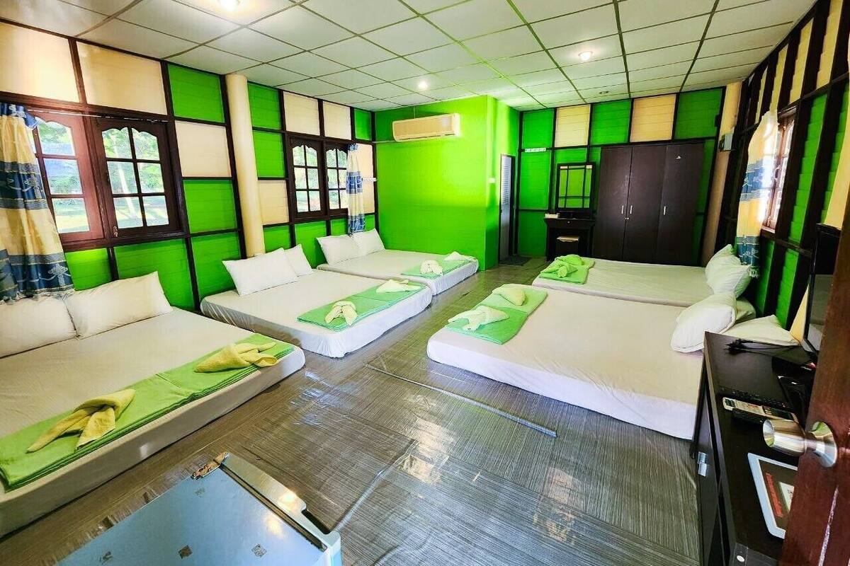 Ein Hotelzimmer mit drei Betten, einem Schrank und einem kleinen Schreibtisch mit Stuhl.
