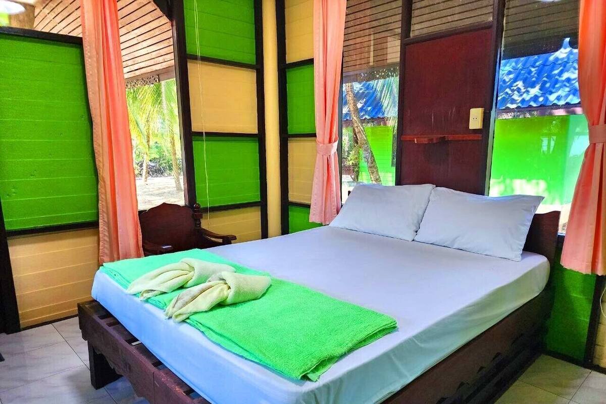 Ein Einzelbett mit einem grünen Handtuch und einem weißen Kissen, eine hölzerne Bank und ein Fenster mit grünen Rollläden.