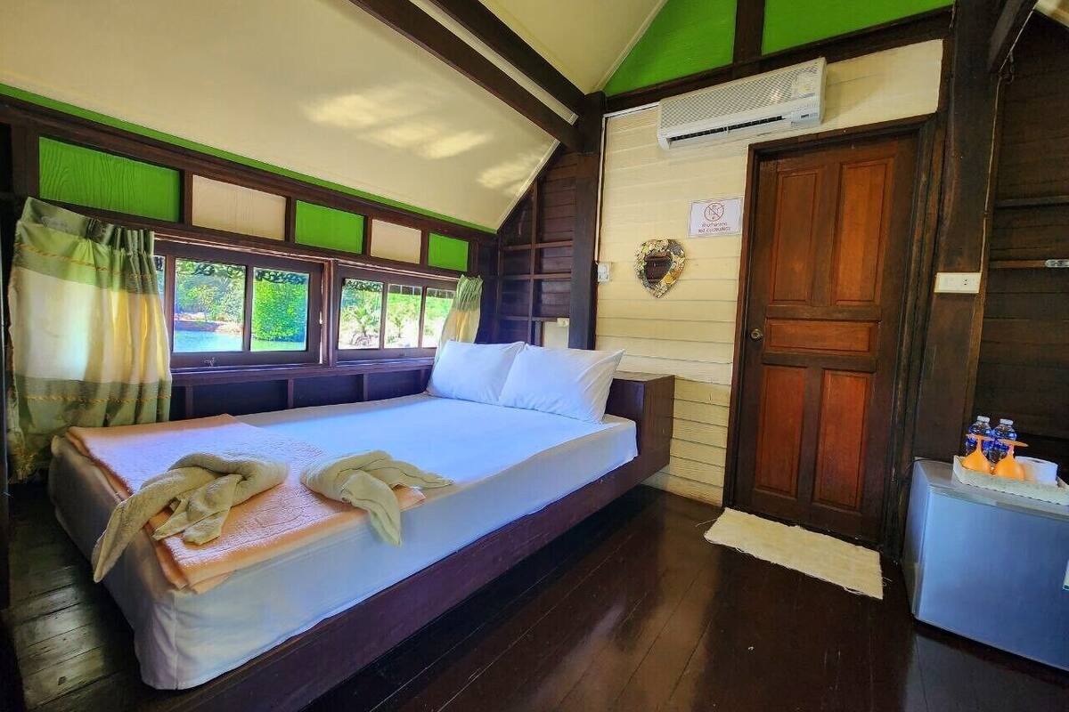 Ein Einzelbett in einem Zimmer mit Holzboden, einer grün-weißen Wand und einer Holztür.