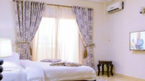 A bedroom with a bed, curtains, a nightstand, a small table, and a wall-mounted air conditioner.