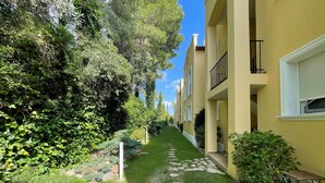 A narrow pathway flanked by lush greenery and yellow buildings with balconies. - Green I - 4A (Pedreguer)