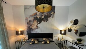 A modern bedroom with a large bed, two bedside tables with lamps, a wall-mounted mirror, and a decorative abstract painting. - Green I - 4A (Pedreguer)