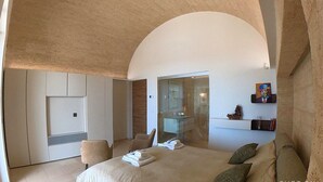 Un dormitorio moderno con una cama grande, una zona de estar y un baño visible a través de un arco.