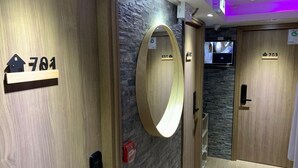 Un pasillo de hotel con paredes de madera, un espejo circular y puertas numeradas.