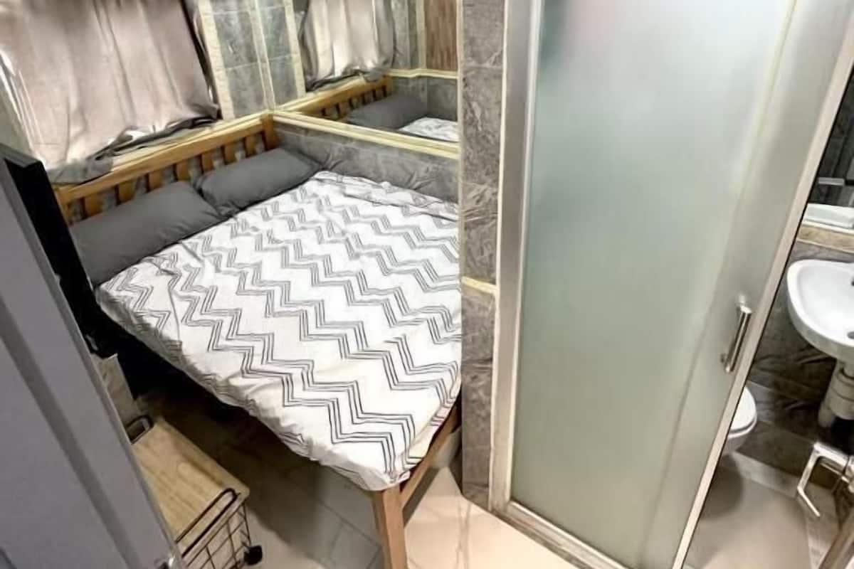 Compact bathroom with shower area, bathtub, and adjacent sleeping space.