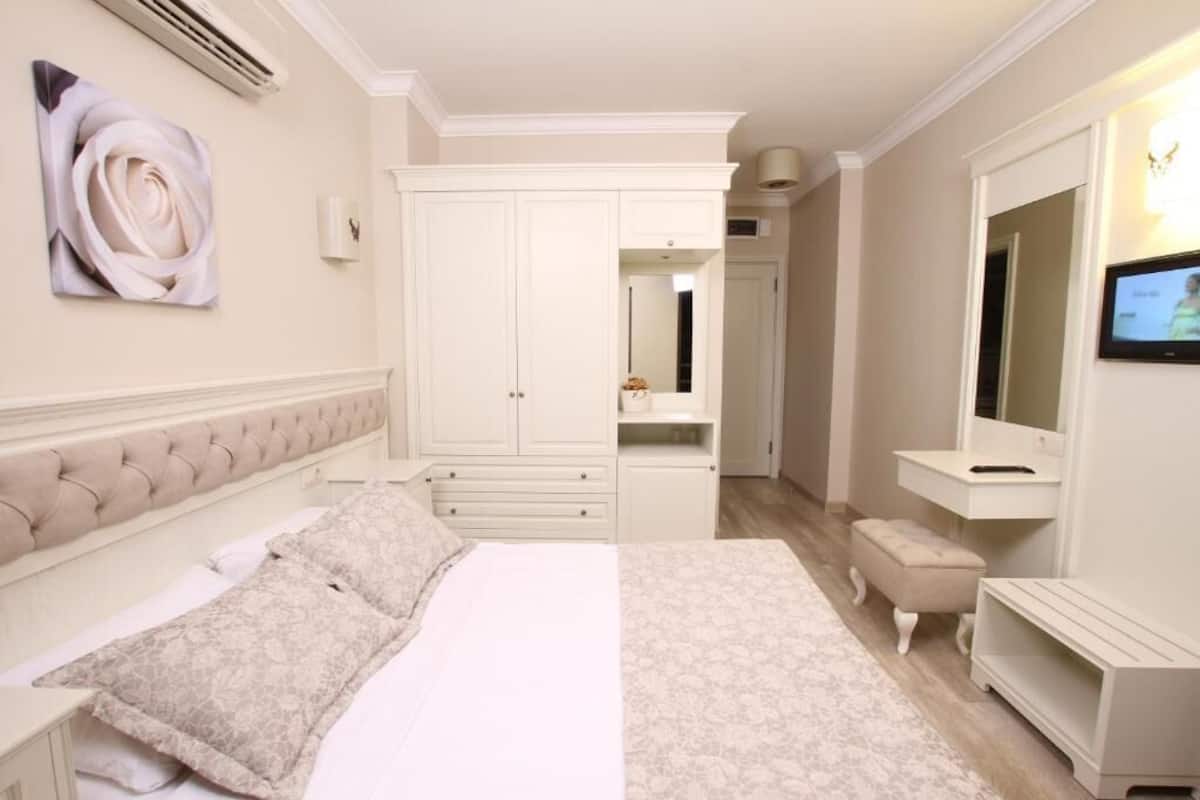 A bedroom with a large bed, a wardrobe, a vanity with a mirror, and a television on the wall.