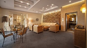 A modern hotel lobby with a stone wall, wicker furniture, and a dining area with a table and chairs. - Hawaii Hotel (Marmaris)