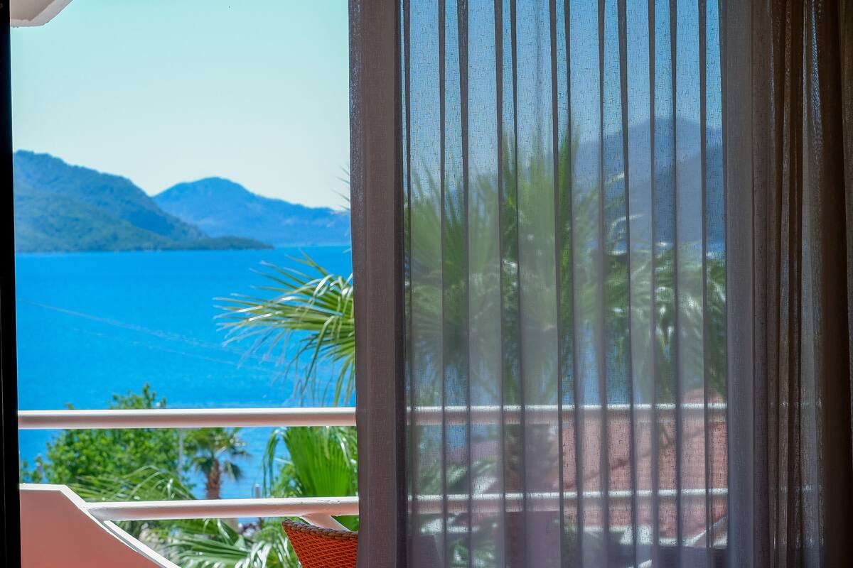 A balcony with a view of a blue body of water, greenery, and distant mountains.