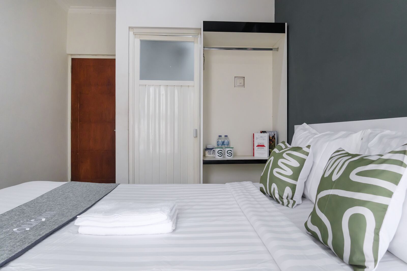 Una habitación de hotel con cama, armario, estante con artículos de aseo y espejo.