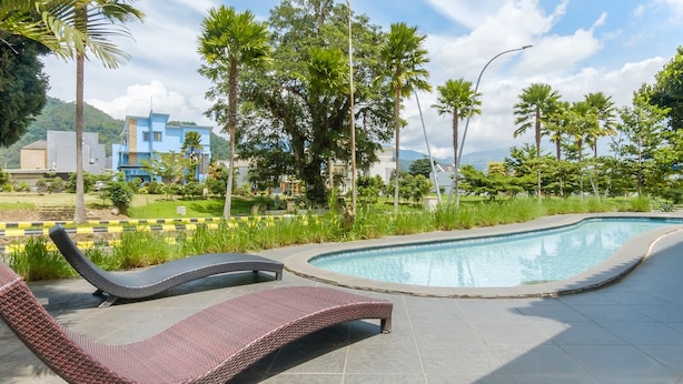 A swimming pool with lounge chairs, surrounded by greenery and buildings in the background. - Mono Coliving Panorama, Batu (Batu)