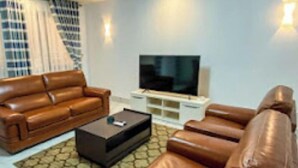 Ein modernes Wohnzimmer mit Ledersofas, einem Flachbildfernseher und einem gemusterten Teppich.