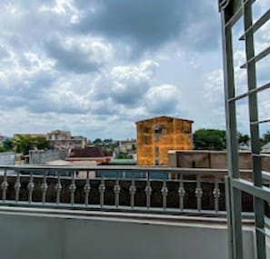Une vue depuis un balcon doté d’une rambarde en métal, donnant sur un paysage urbain composé de différents bâtiments, dont une imposante structure jaune.