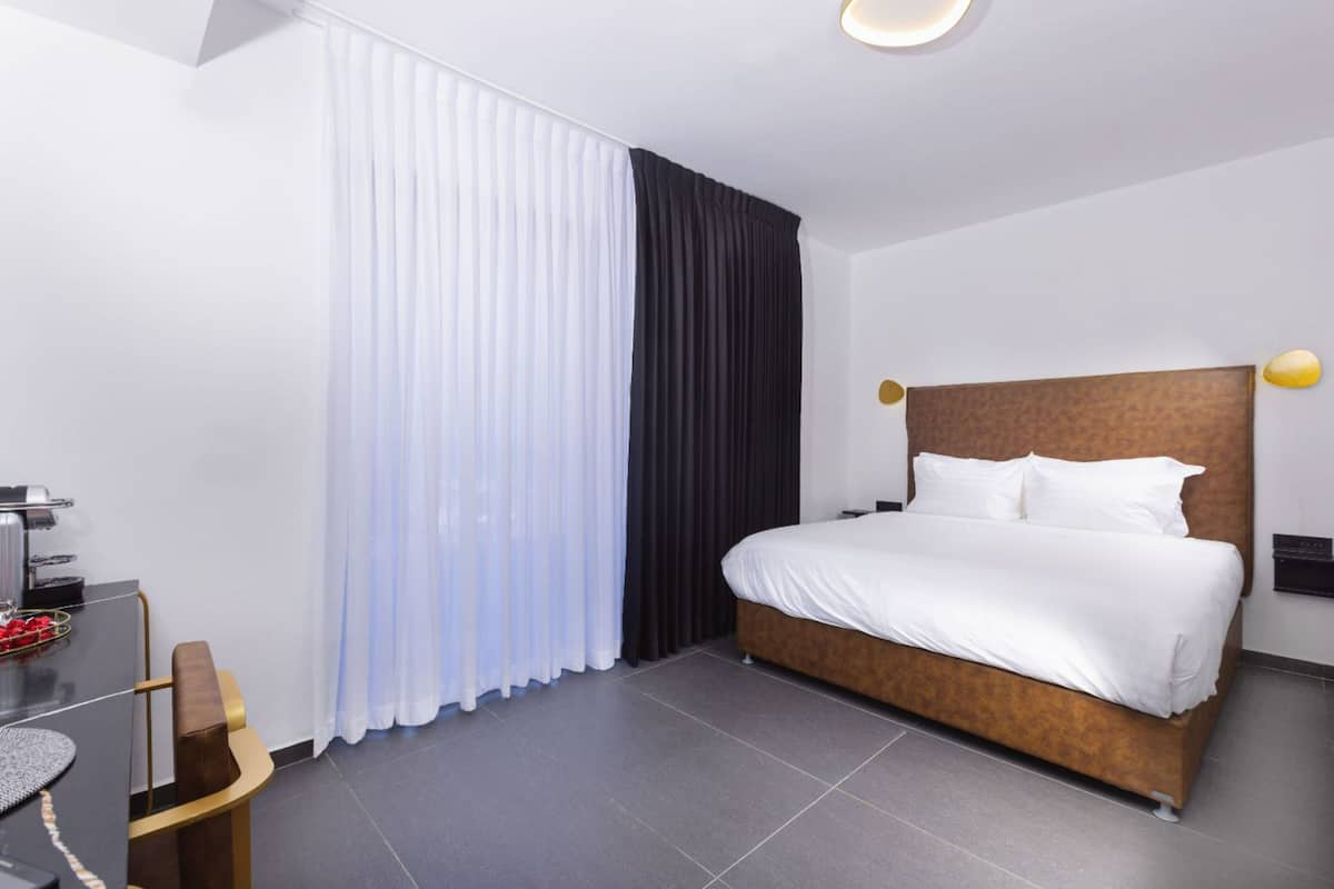 Una habitación de hotel moderna con una cama grande, un escritorio con silla y una ventana con cortinas traslúcidas.