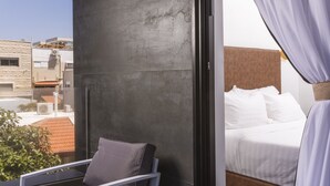 Habitación de hotel moderna con balcón, cama con ropa blanca y vista a la ciudad.