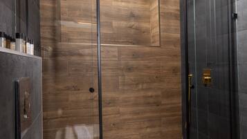 A modern bathroom with a glass-enclosed shower, wooden flooring, and a white toilet.