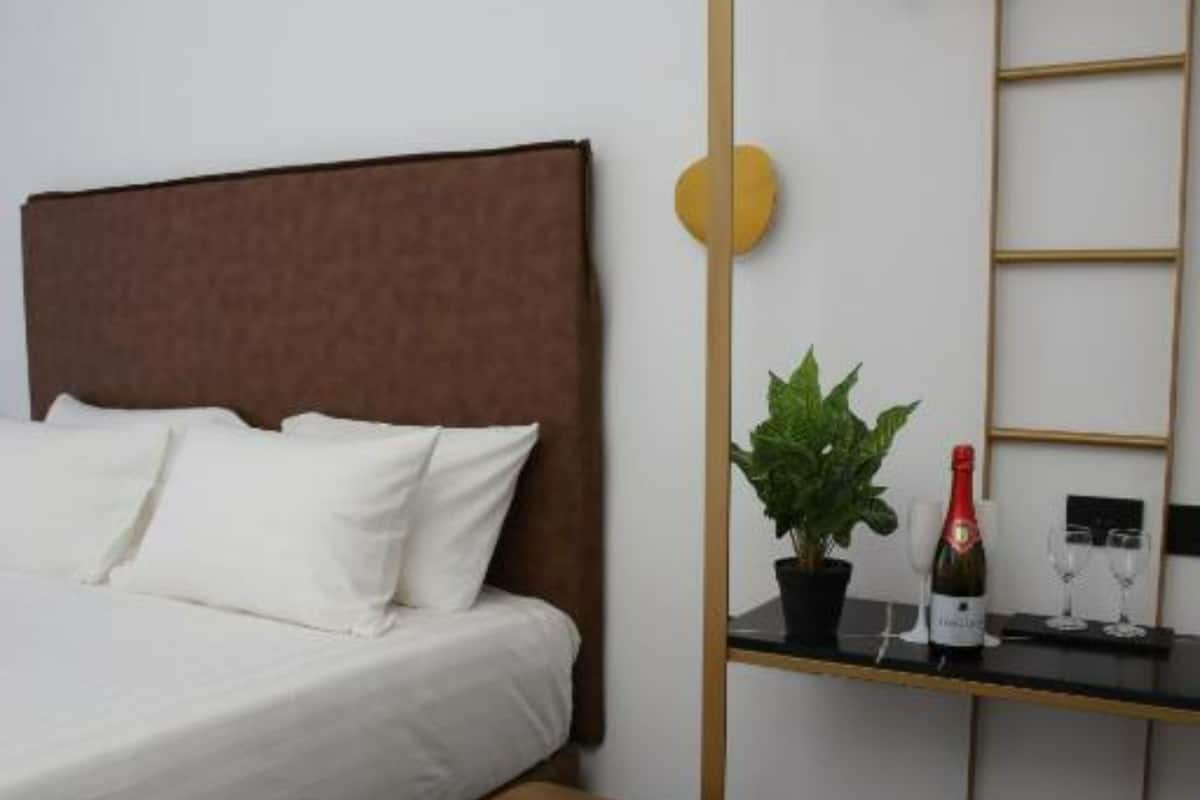 Una habitación de hotel moderna con una cama, un taburete pequeño, una planta, una botella de vino y una escalera apoyada en la pared.