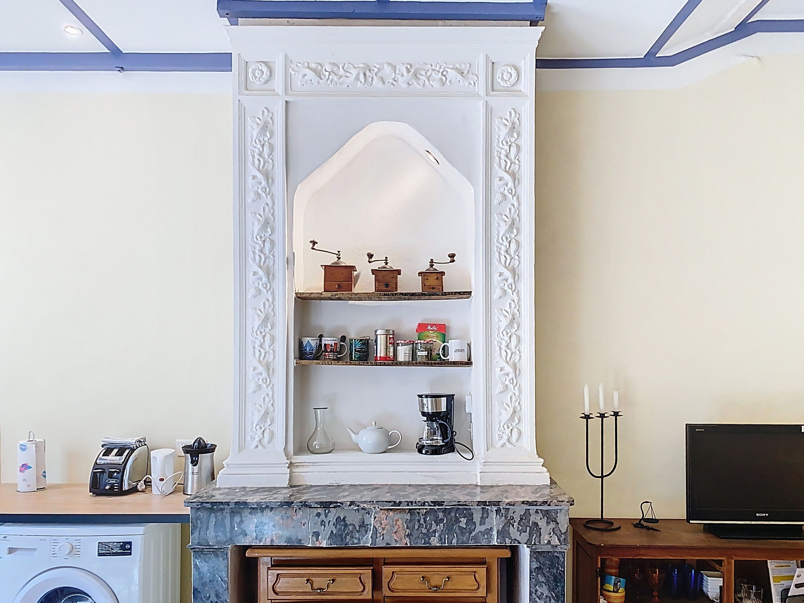 Une cuisine avec une cheminée décorative blanche, une machine à café et un grille-pain posés sur le plan de travail.