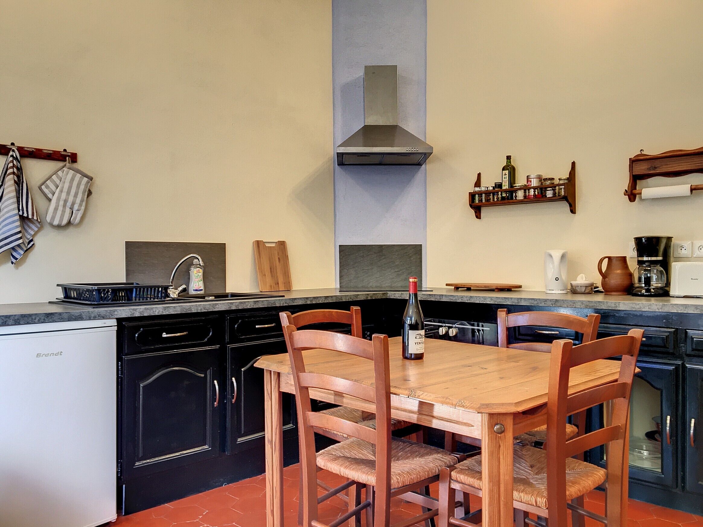 Une cuisine avec une table et des chaises en bois, un lave-vaisselle, une cuisinière et une bouteille de vin.