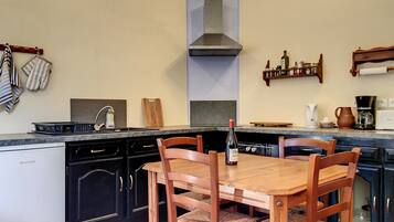 Une cuisine avec une table et des chaises en bois, un lave-vaisselle, une cuisinière et une bouteille de vin.