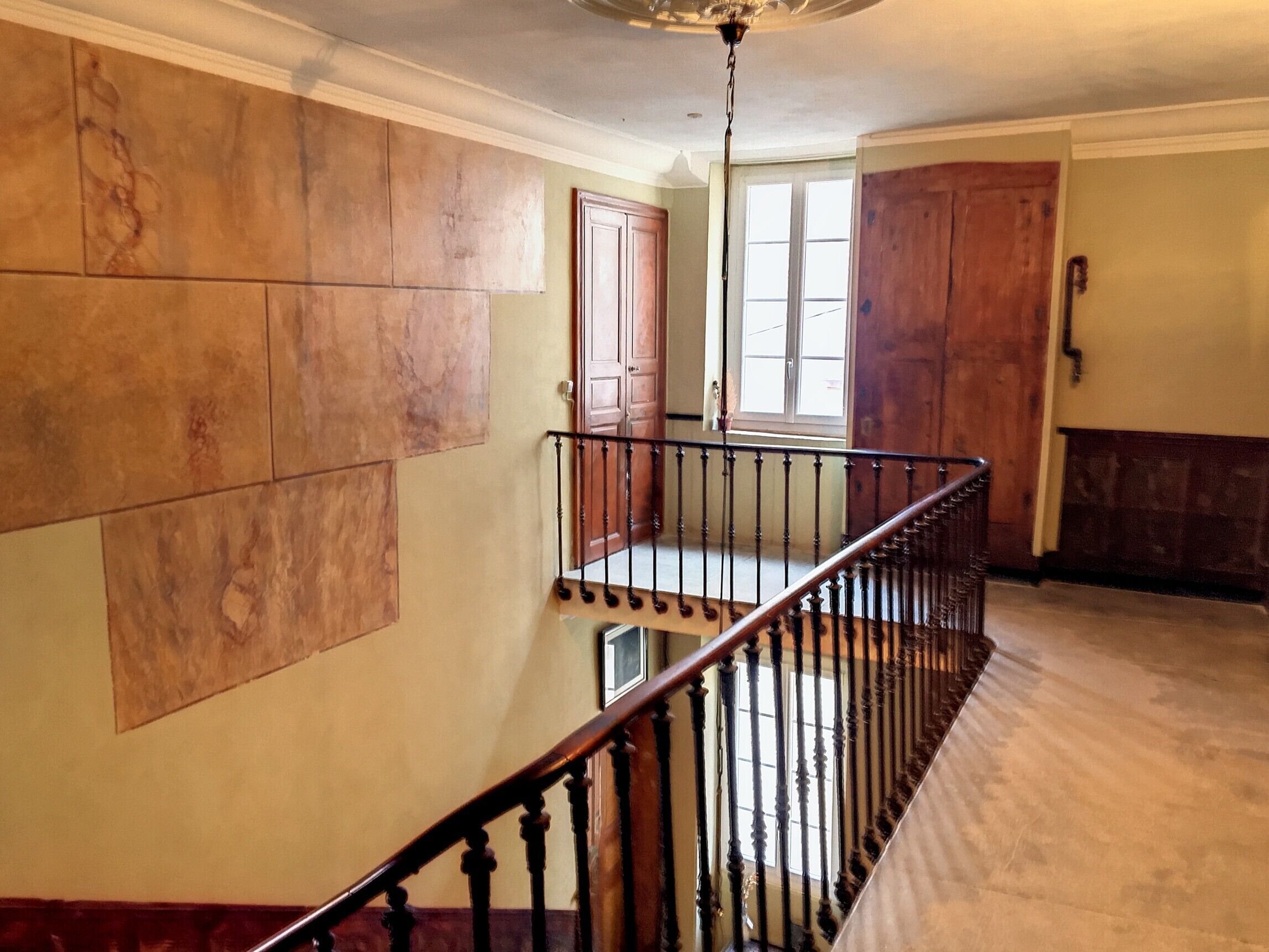 Una escalera con barandilla de madera y balaustres negros, que lleva a una plataforma con vistas a una puerta y una ventana.