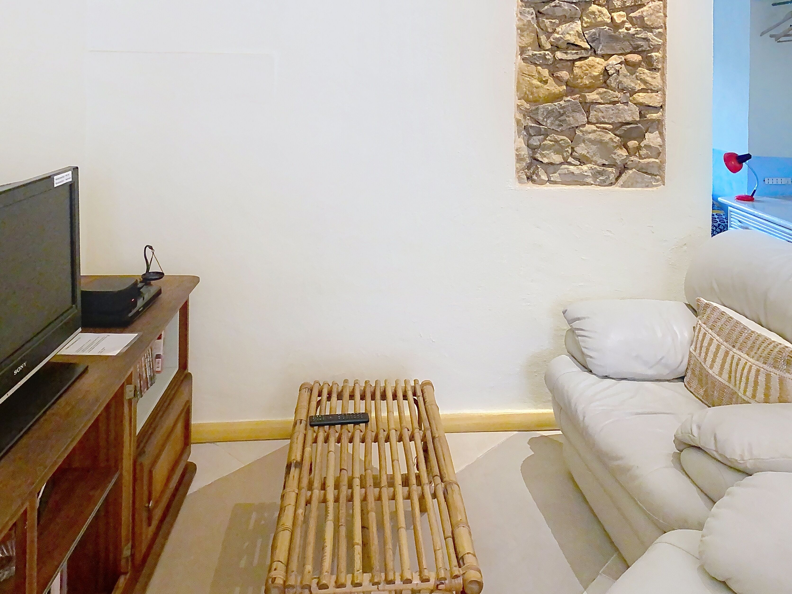 Una sala de estar con una televisión sobre un mueble de madera, una pared de piedra y un sofá blanco con cojines.