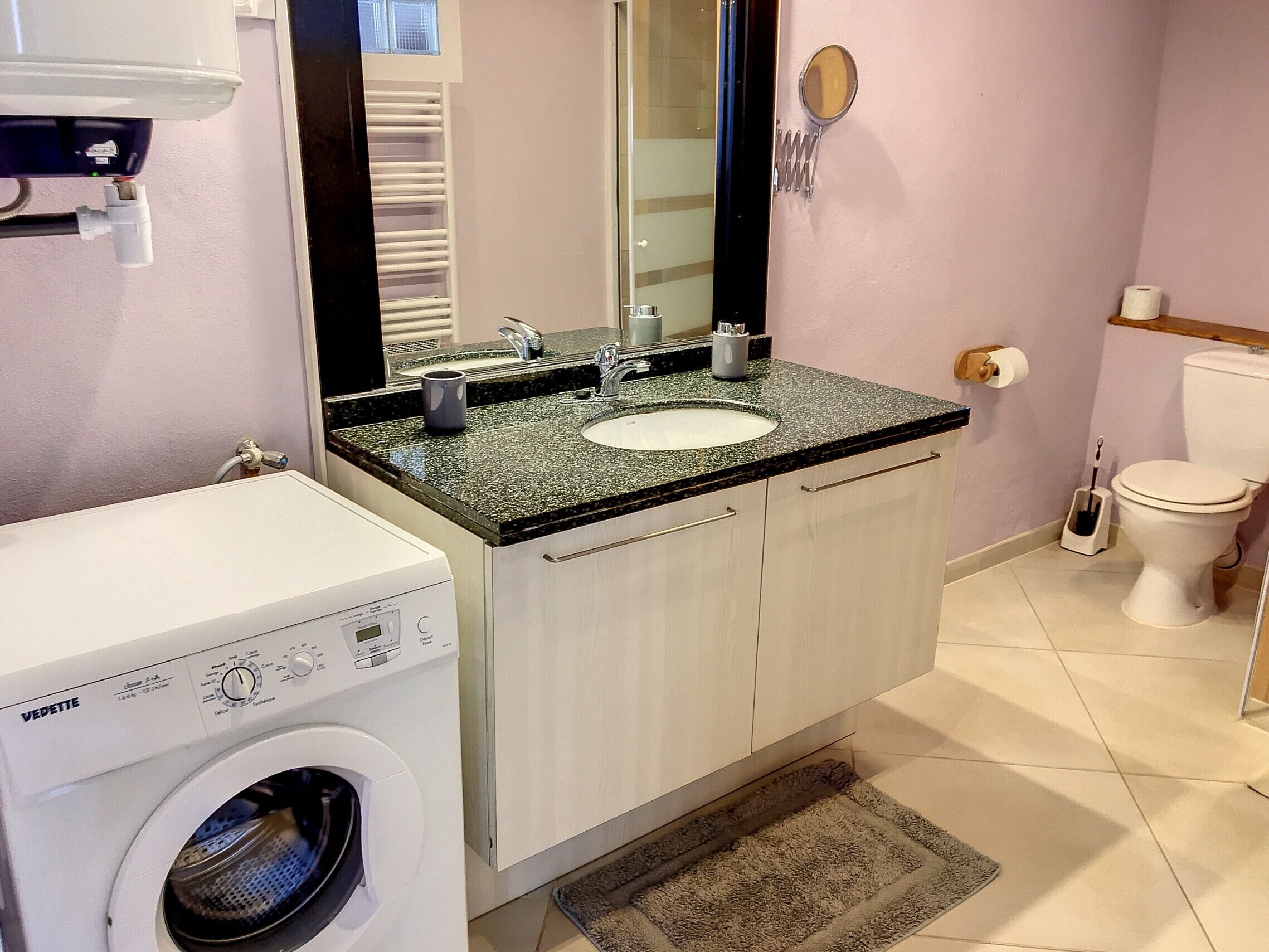 Un baño pequeño con lavadora, un lavabo con espejo y un inodoro.