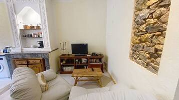 Una sala de estar con una pared de piedra, un televisor sobre un mueble de madera y un sofá.