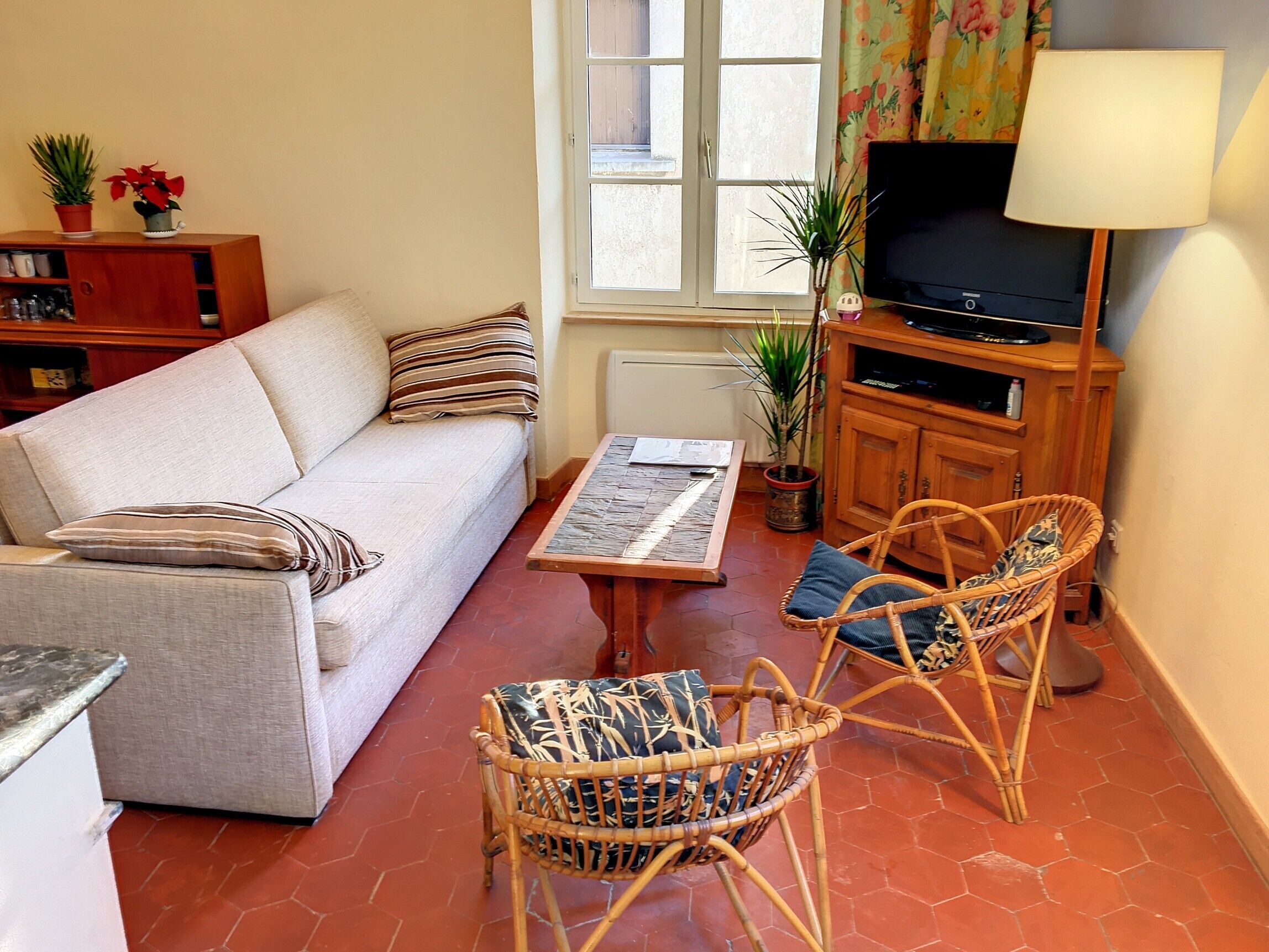 A living room with a sofa, two wicker chairs, a coffee table, a television, and a window with curtains.