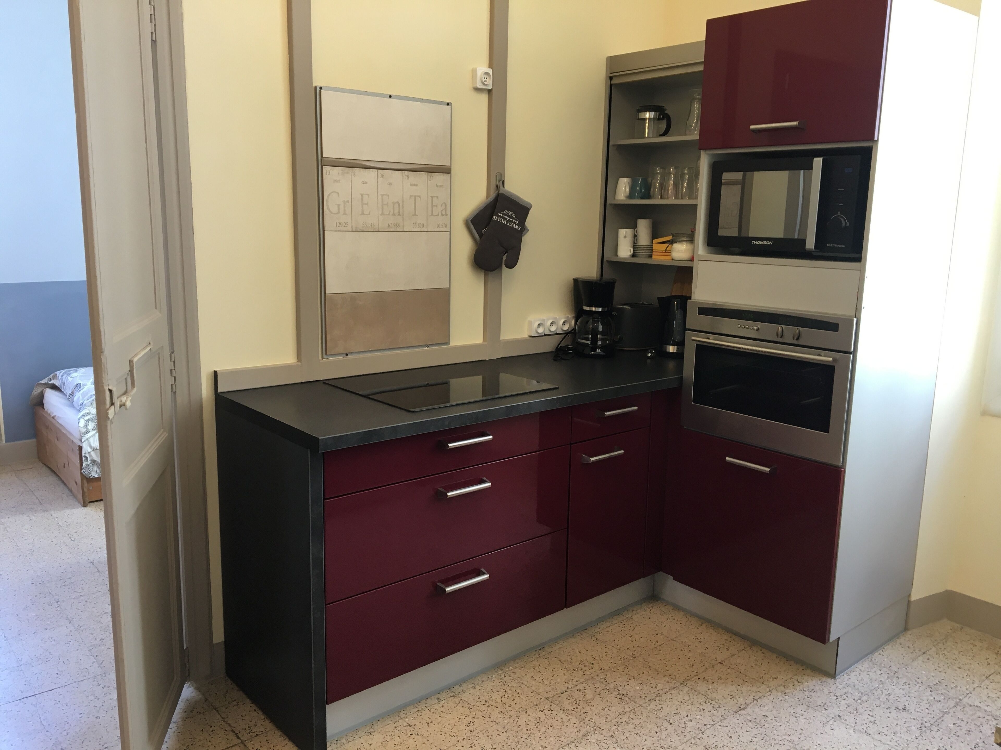 Een kleine keuken met een zwart aanrecht, roestvrijstalen apparatuur en donkerrode kastjes.