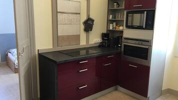 Een kleine keuken met een zwart aanrecht, roestvrijstalen apparatuur en donkerrode kastjes.