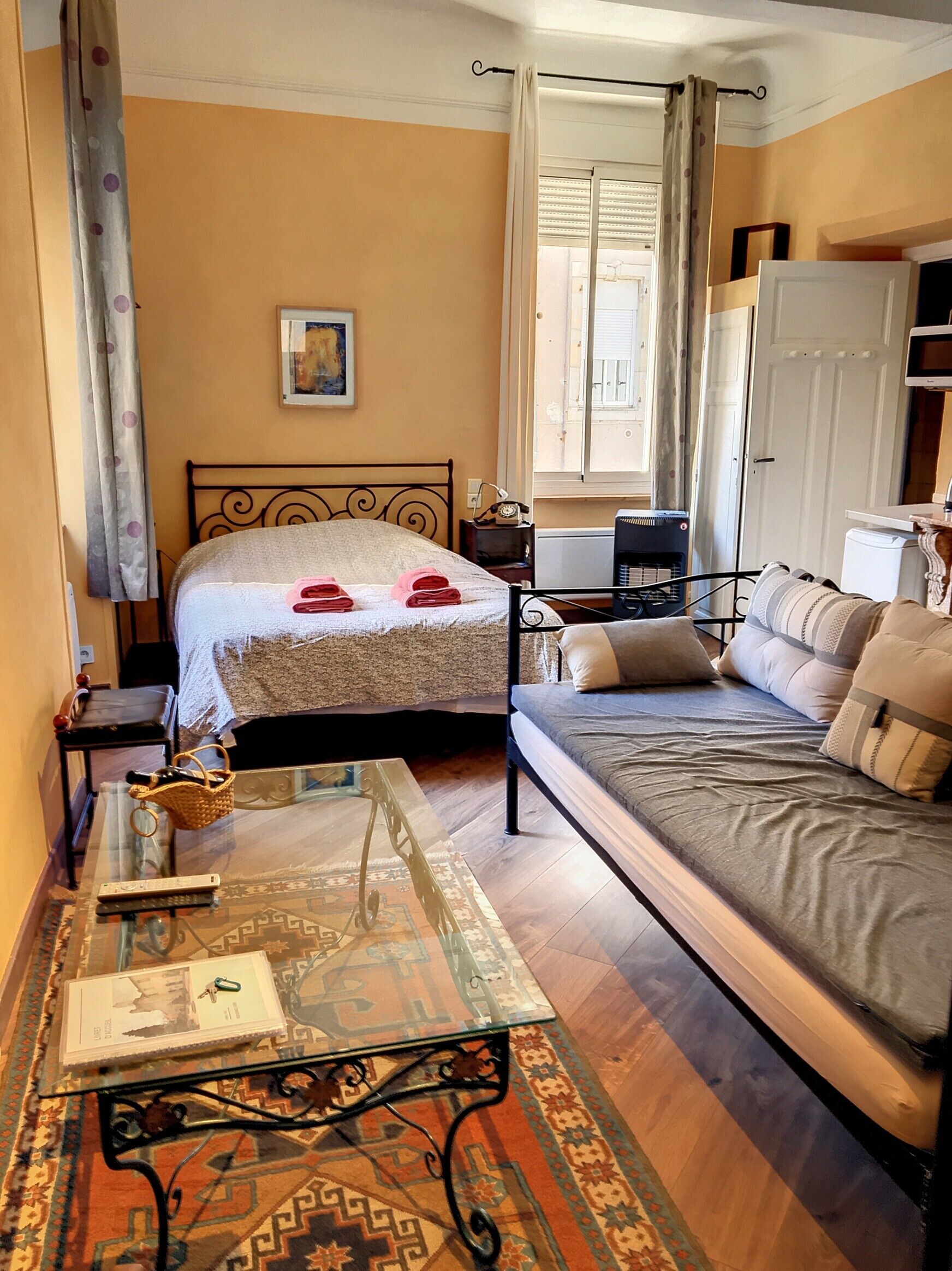 A cozy bedroom with a bed, a sofa, a small table, and a window with curtains.