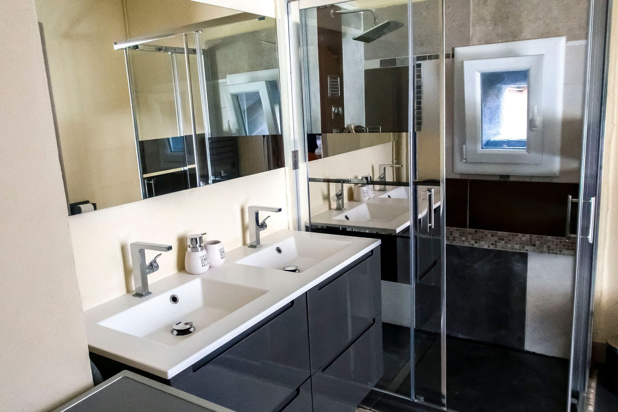 A modern bathroom with two sinks, a large mirror, and a shower.