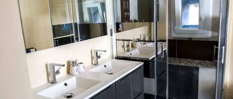 Un baño moderno con dos lavamanos, un espejo grande y una ducha.