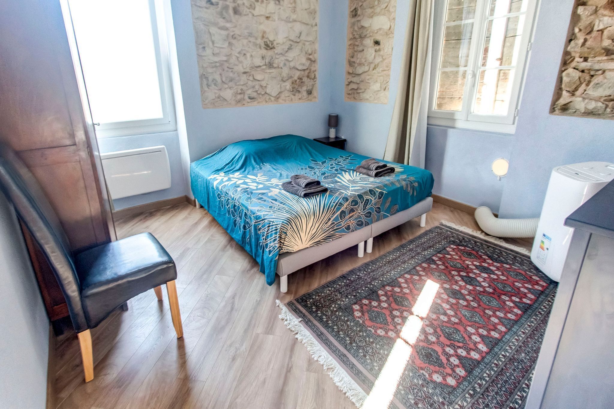 Ein Schlafzimmer mit einem Bett, einem Sessel, einem Heizlüfter, einer Heizung und einem Fenster.