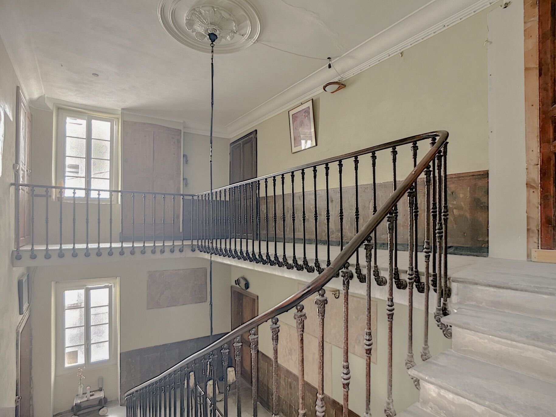 Ein mehrgeschossiges Interieur mit einer zentralen Treppe, einem Deckenventilator und einem Fenster im Obergeschoss.