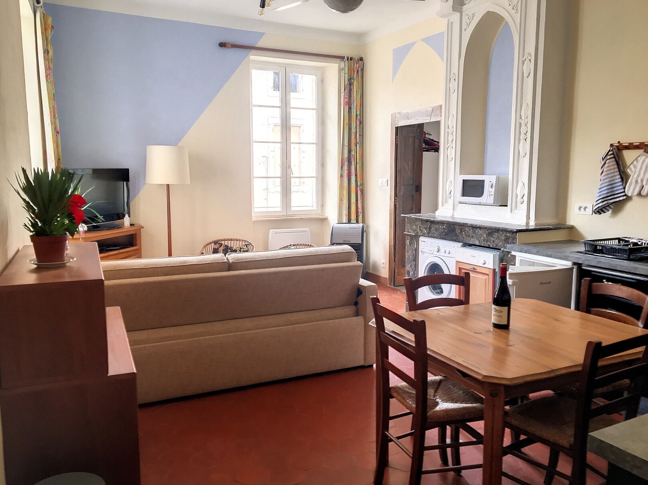 A compact living space with a sofa, a dining table, and a kitchen area including a washing machine.
