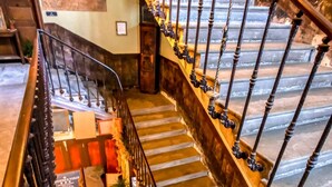 A grand staircase with ornate railings and a chandelier, leading to a landing area with a patterned floor and a small plant. - Résidence Verdi (Bedarieux)