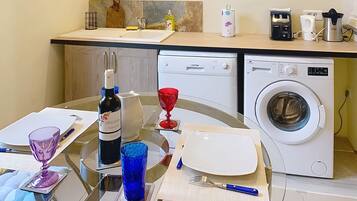Una cocina con lavadora, una botella de vino y una mesa de comedor dispuesta con platos, vasos y cubiertos.
