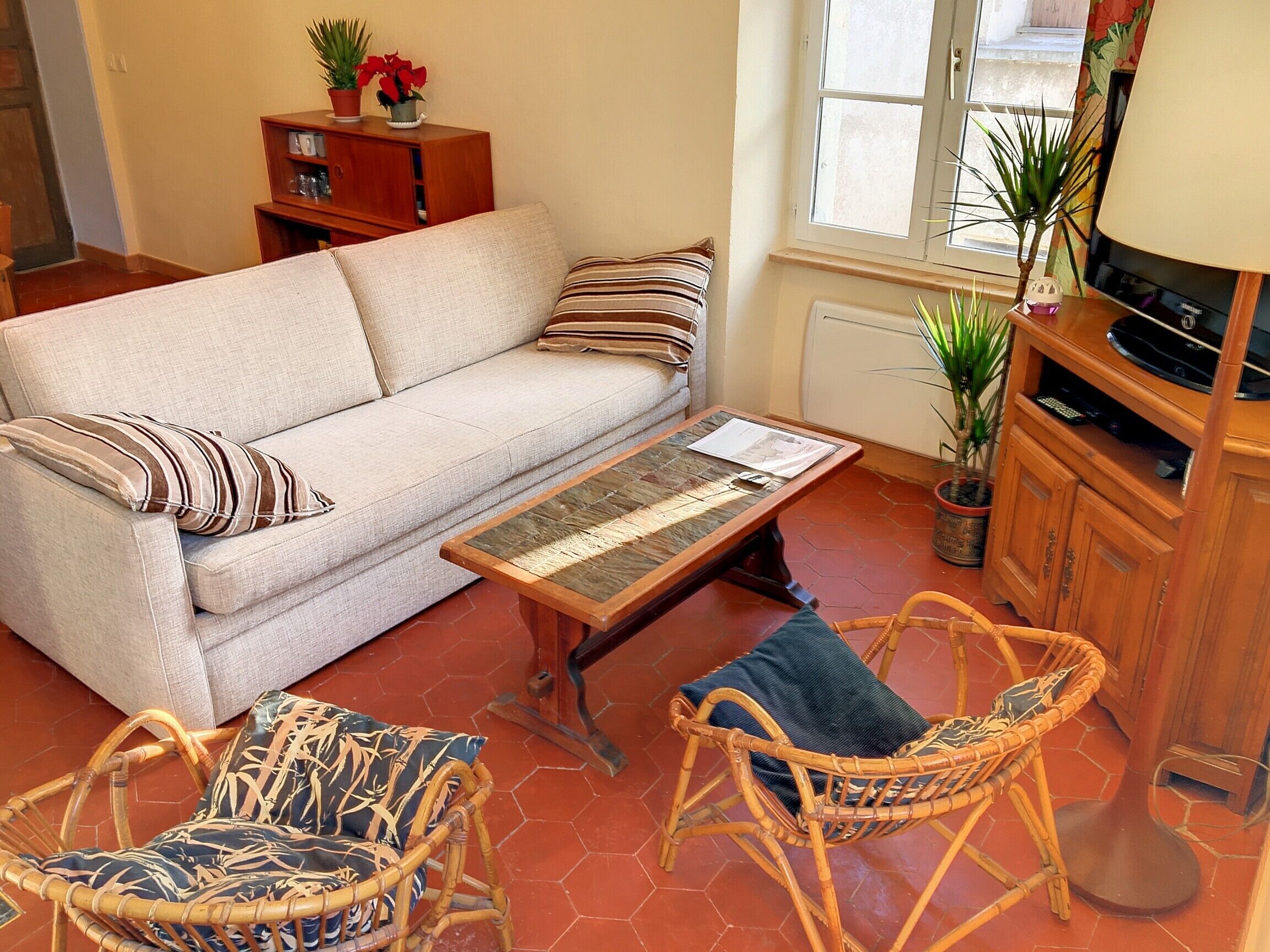 A living room with a sofa, two wicker chairs, a coffee table, a wooden cabinet, and a potted plant.