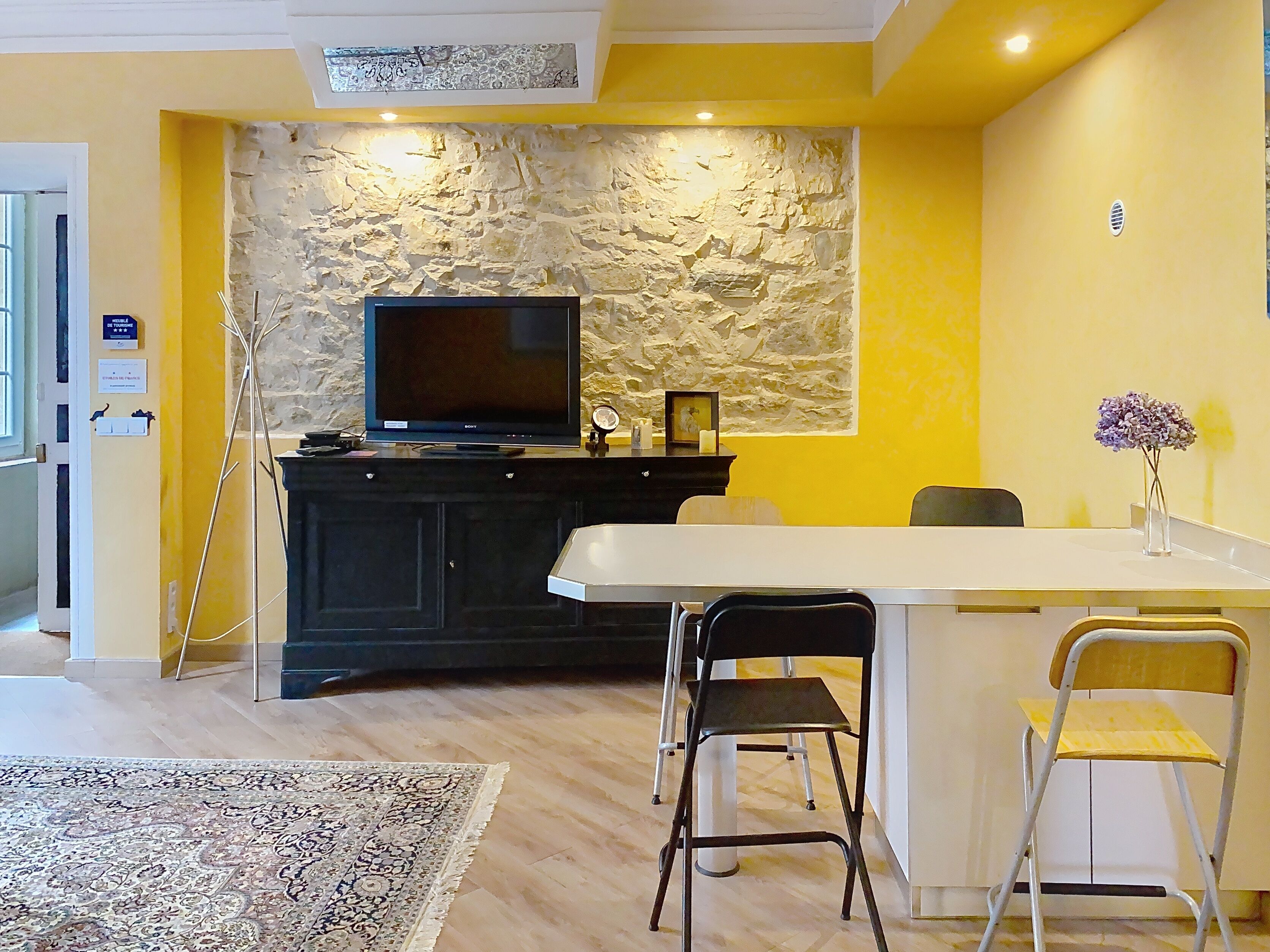 Una sala de estar moderna con una pared de acento de piedra, un televisor de pantalla plana, una mesa de comedor con sillas y una alfombra estampada.