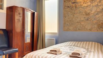 Een slaapkamer met een bed, een houten garderobe, een stoel, een raam met gordijnen en een stenen muur.