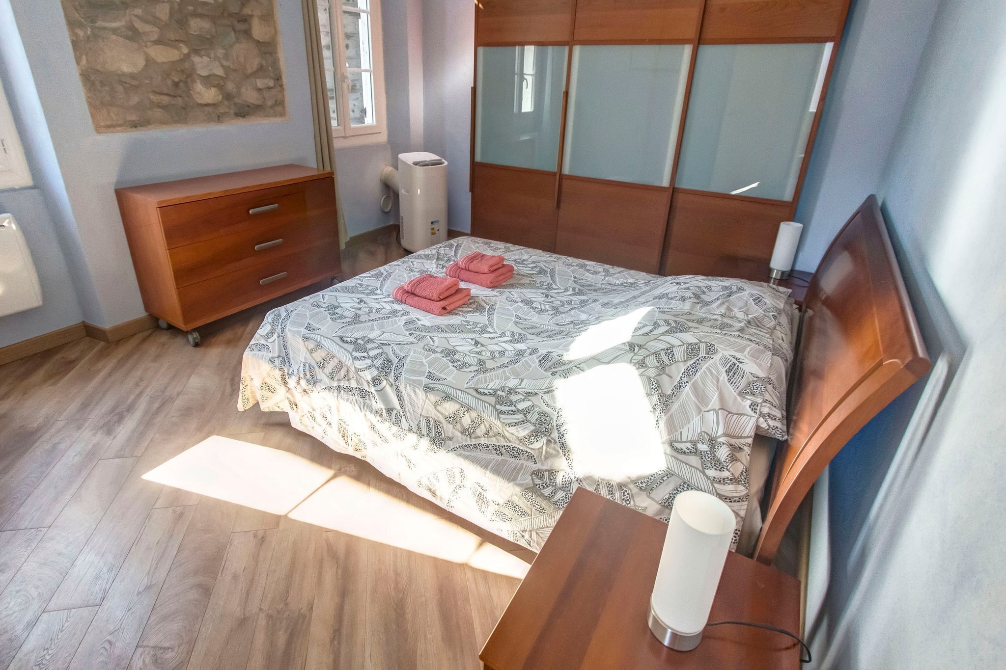 Ein Schlafzimmer mit einem Bett, einem Holzschrank und einem Nachttisch mit Lampe.