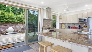 A modern kitchen with a large island, stainless steel appliances, and a sliding glass door to the backyard. - Donlen Cottage Wentworth Falls 180 Degree Views (WENTWORTH FALLS)