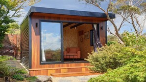 A modern cabin with a glass door, wooden exterior, and a small seating area inside. - Donlen Cottage Wentworth Falls 180 Degree Views (WENTWORTH FALLS)