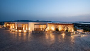 A modern building with multiple rooms and a stone facade, located on a spacious terrace with a view of the sea and mountains. - Utopia Suites by Anna Platanou - Adults only (Paros)