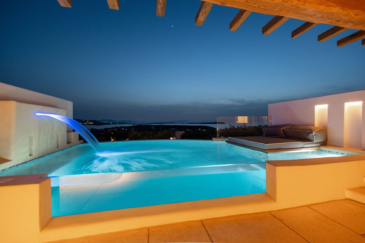 A modern outdoor pool area with a hot tub, a wooden pergola, and a seating area with cushions.